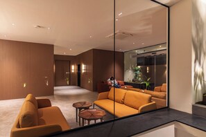 A modern interior with a sofa, chairs, a coffee table, and a large mirror reflecting a room with a plant and a window. - Hotel Starlight by Avana (Hyderabad)