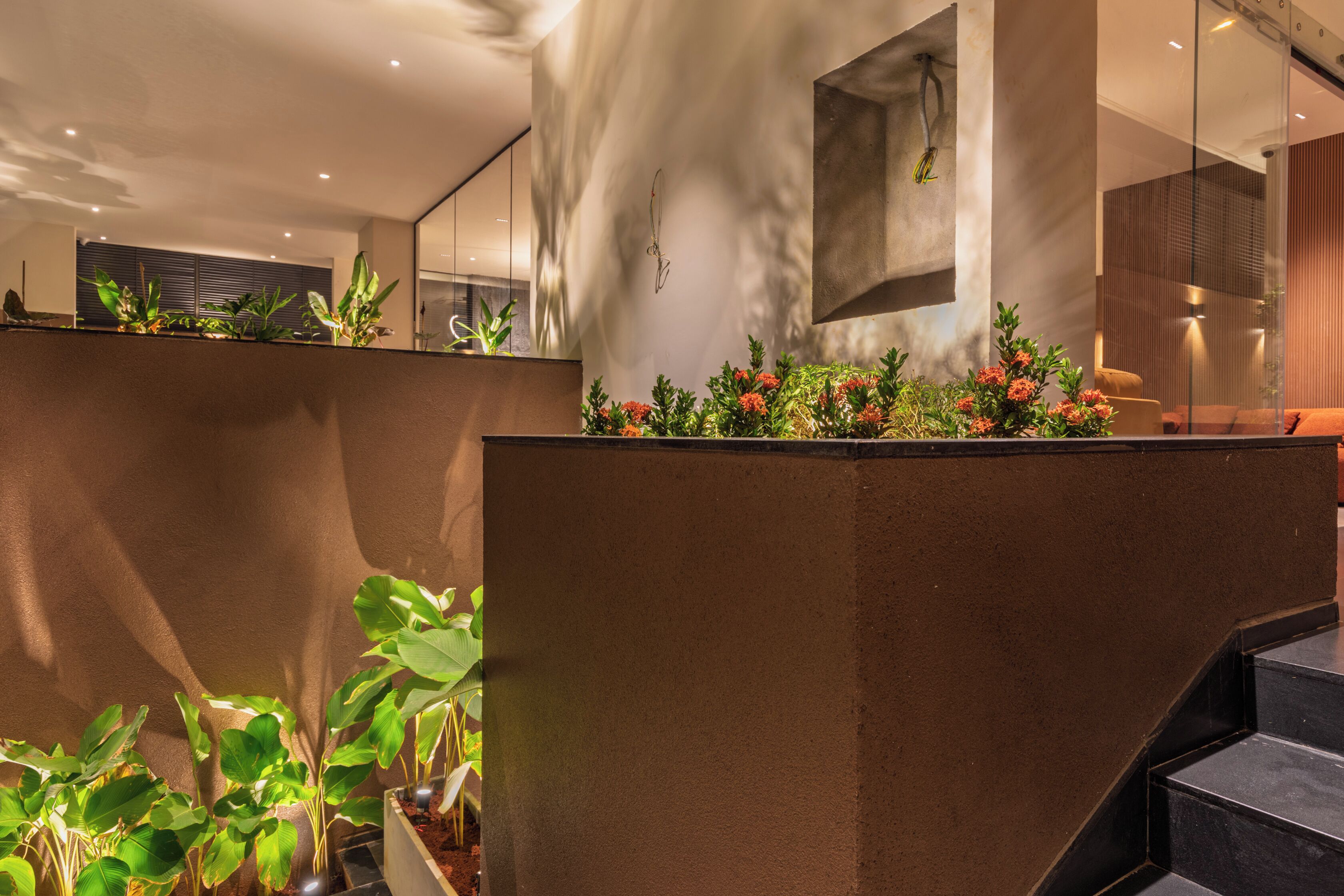 Un interior moderno con una escalera, una lámpara fijada a la pared y plantas en macetas.
