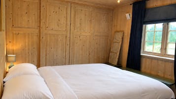 Habitación con paneles de madera, una cama, una mesita de noche y un ventanal con cortinas.