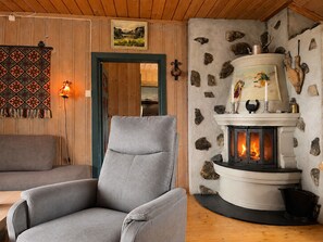 Una habitación acogedora con chimenea de piedra, un sillón gris y una alfombra estampada.