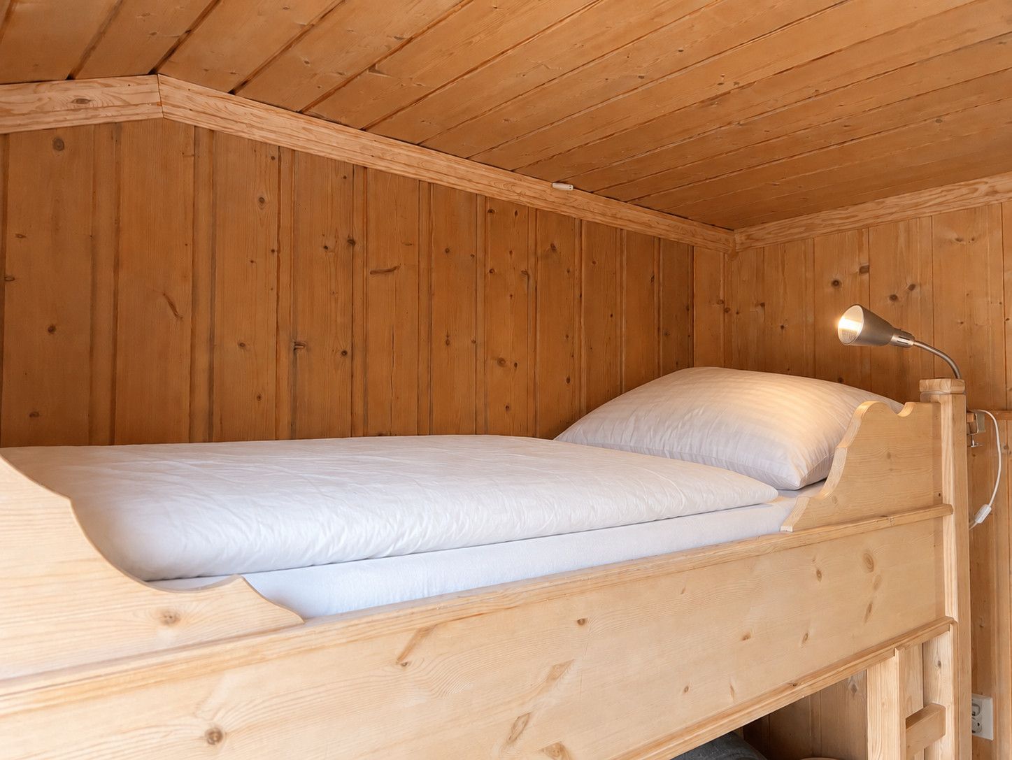Un simple lit superposé en bois, avec une tête de lit et une lampe de chevet.