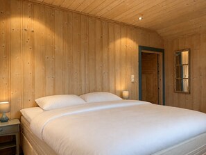 Una habitación con paneles de madera, una cama, dos lámparas de noche y una puerta con espejo.