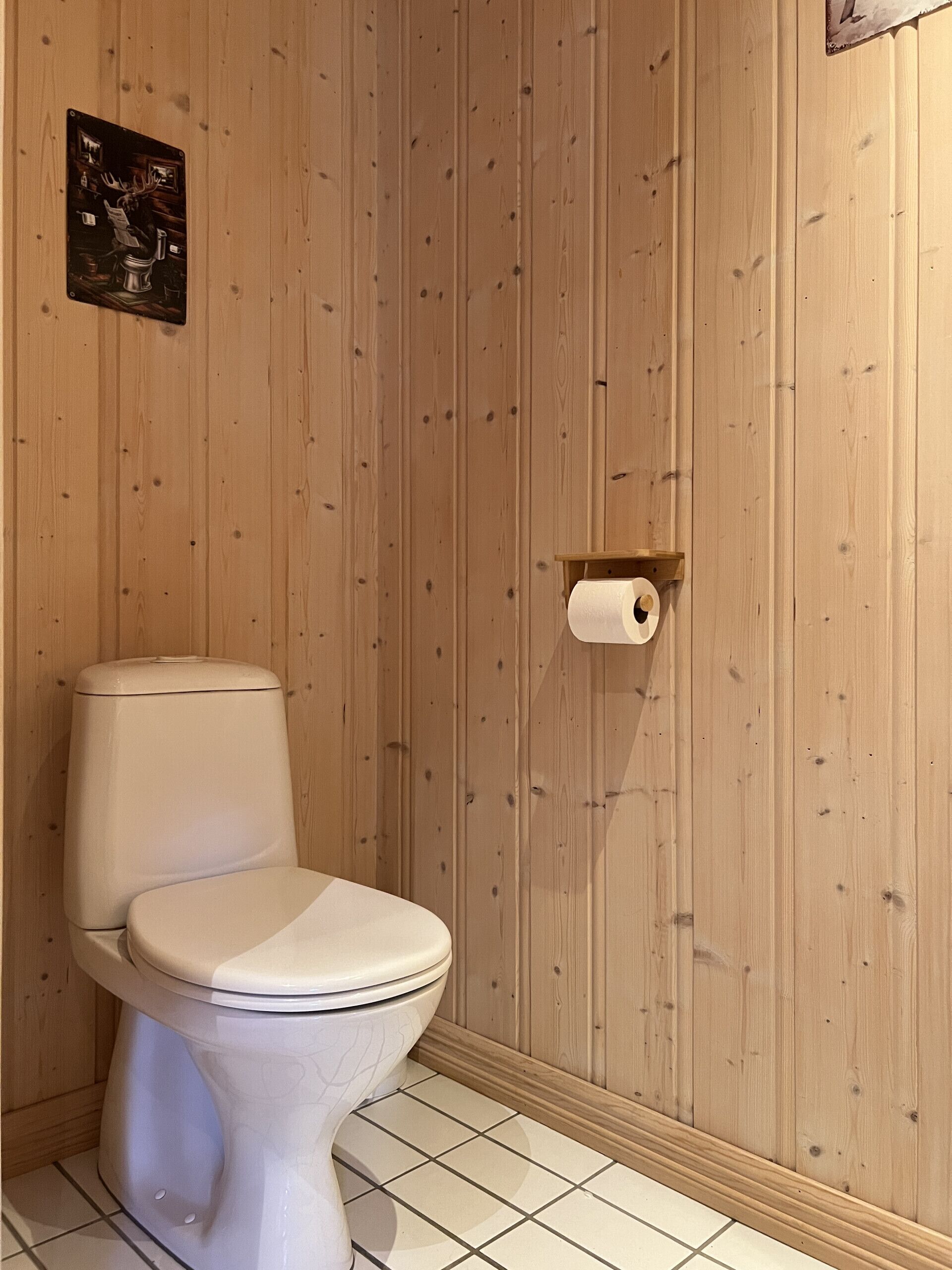 Un baño con inodoro, pared de madera y dispensador de papel higiénico.