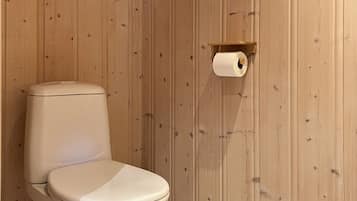 Un baño con inodoro, pared de madera y dispensador de papel higiénico.