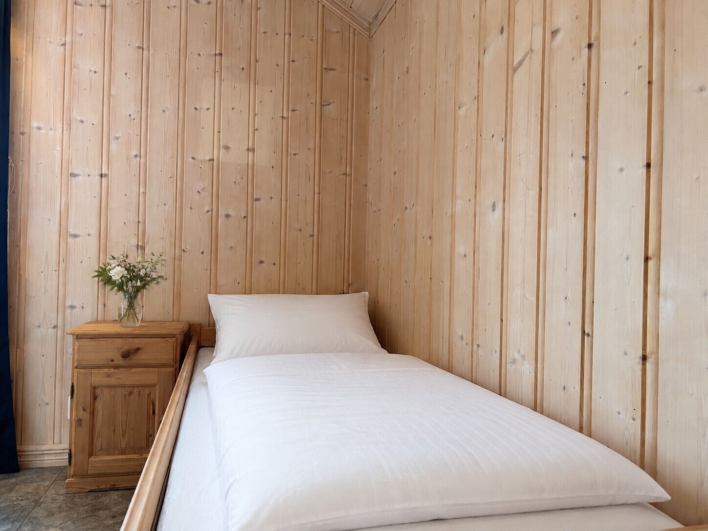 Un letto singolo con biancheria da letto bianca in una stanza con pareti rivestite in legno.