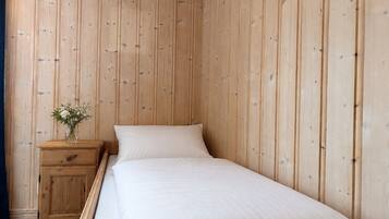 Un letto singolo con biancheria da letto bianca in una stanza con pareti rivestite in legno.
