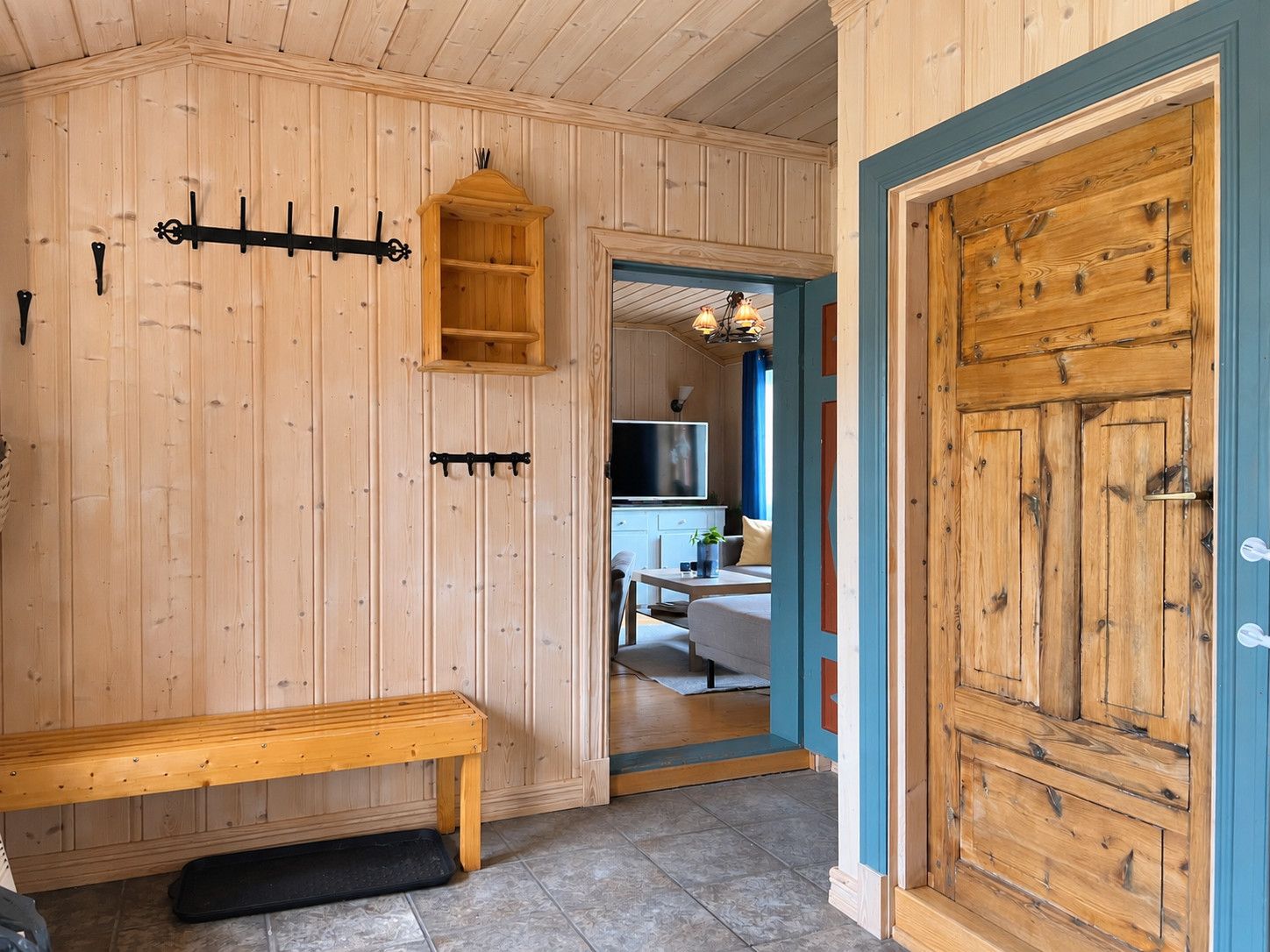 A wooden interior with a bench, a wooden cabinet, and a door leading to another room.