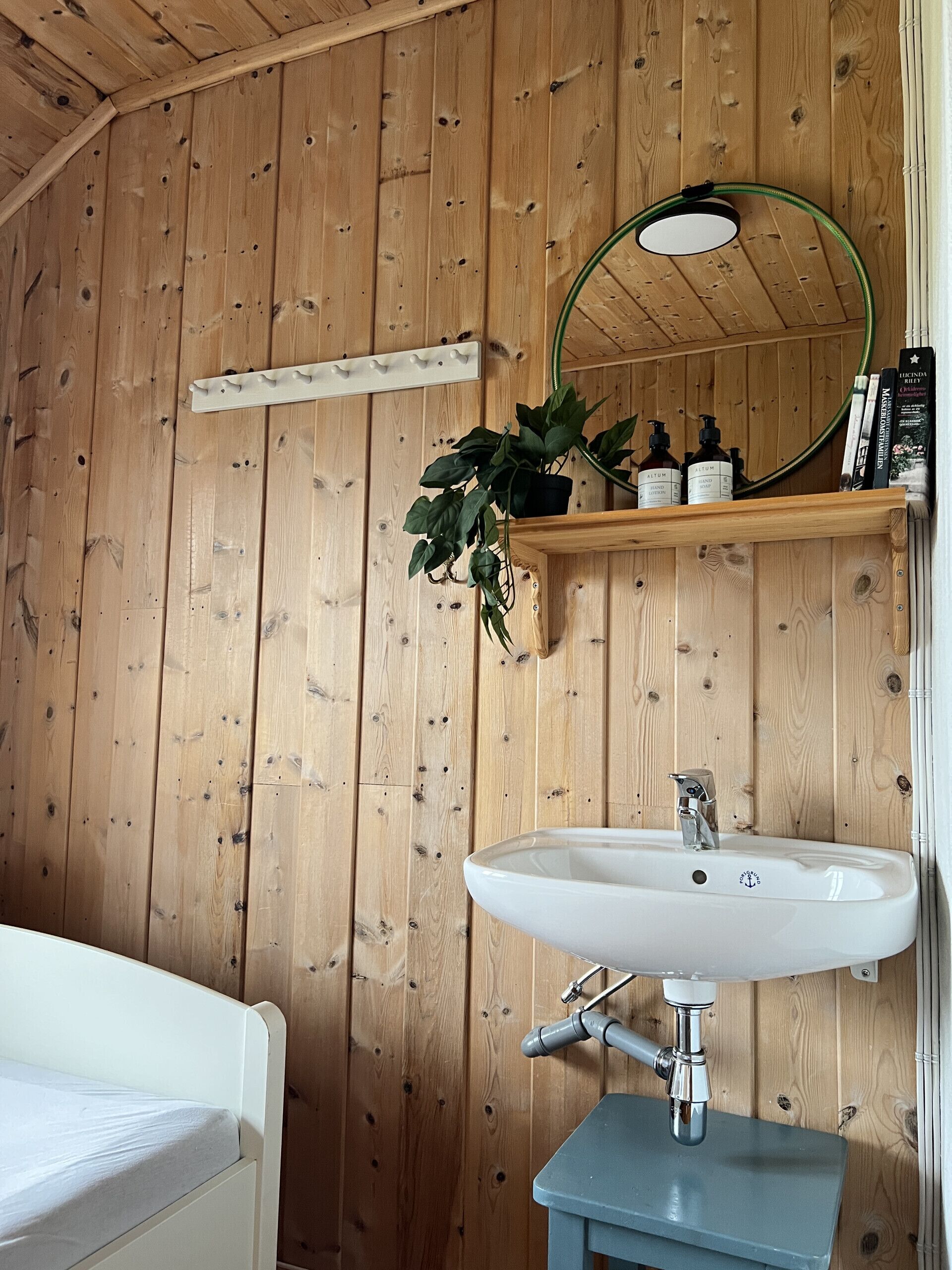 Un intérieur en bois avec un lavabo blanc, un miroir et une étagère contenant des articles de toilette.