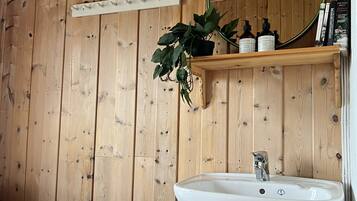 Un intérieur en bois avec un lavabo blanc, un miroir et une étagère contenant des articles de toilette.