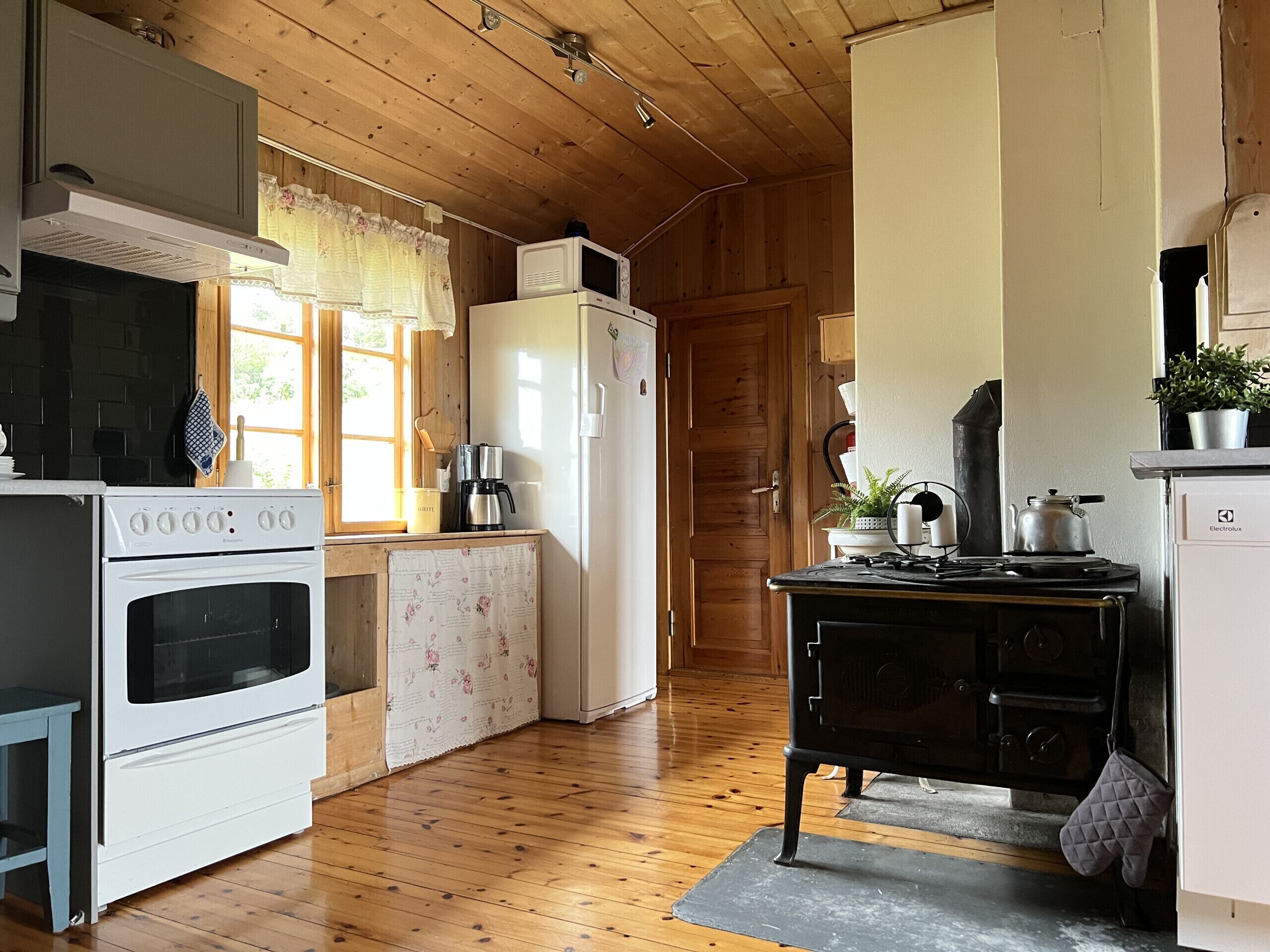 A kitchen with wooden flooring, a stove, a refrigerator, and a black stove top.