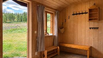 A wooden interior with a bench, a window with curtains, and a wall-mounted rack.