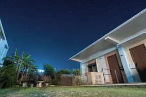 A residential building with a garage door, a small garden with plants, and a clear night sky with stars. - Bella yui Miyakojima 2 (Higashinakasone,Hirara,Miyakojima)