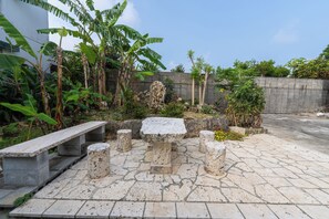 A stone patio with a bench and stone stools, surrounded by tropical plants and a concrete wall. - Bella yui Miyakojima 2 (Higashinakasone,Hirara,Miyakojima)