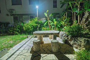 An outdoor seating area with a stone table and four stools, surrounded by lush greenery and a stone-paved walkway. - Bella yui Miyakojima 2 (Higashinakasone,Hirara,Miyakojima)