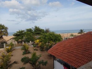 A beach view with a red-roofed building in the foreground, palm trees, and a sandy area. - Salt & sand resort (Arugam Bay)