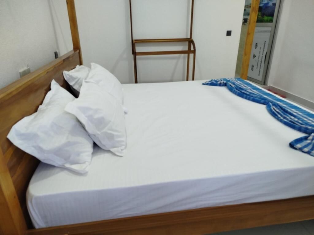 A single bed with a wooden frame, white bedding, and a blue patterned blanket.