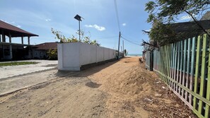 A paved pathway leading to a building with a covered entrance, a sandy area beside the path, and a fence with vertical slats. - Salt & sand resort (Arugam Bay)