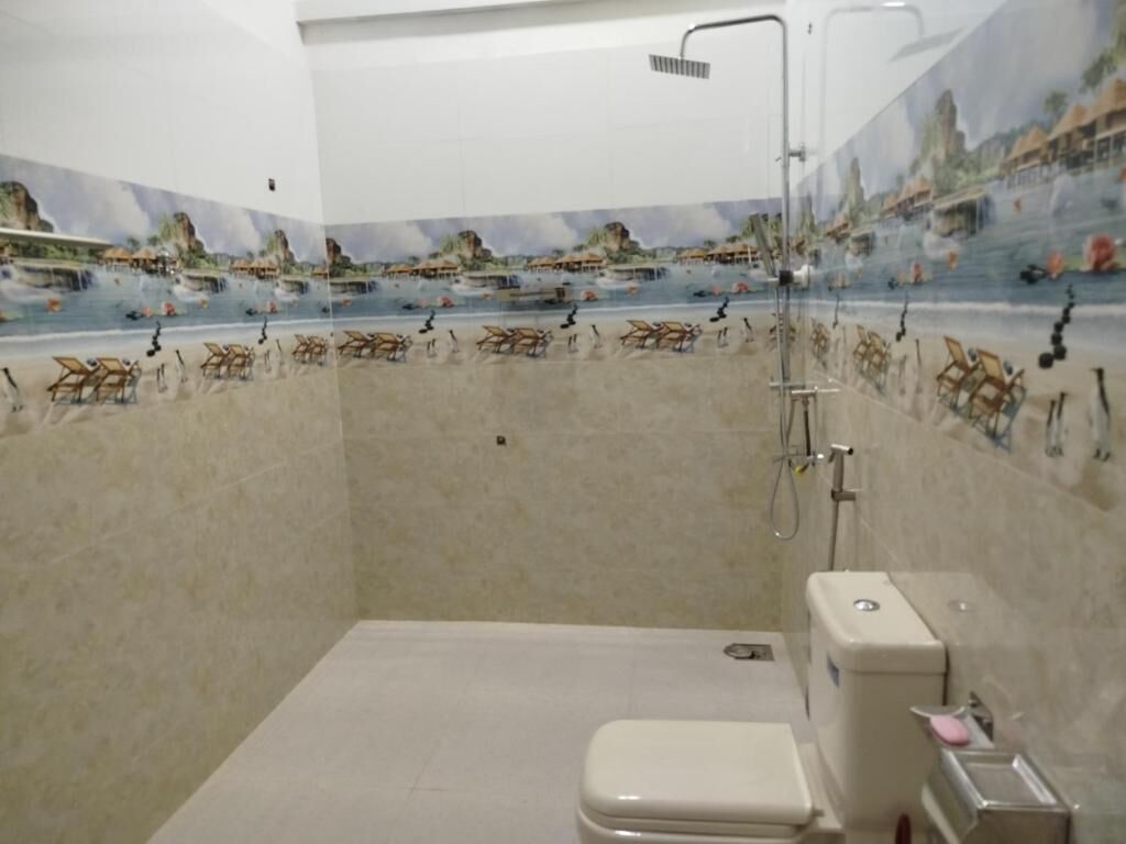 Casa de banho com chuveiro, sanita e um mural decorativo nas paredes.