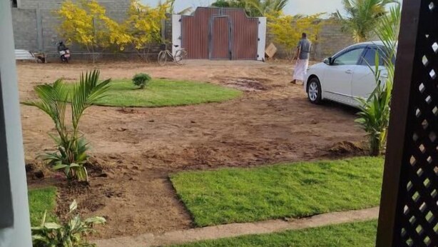 Vista de un patio con un automóvil blanco estacionado, una persona caminando y un edificio al fondo.