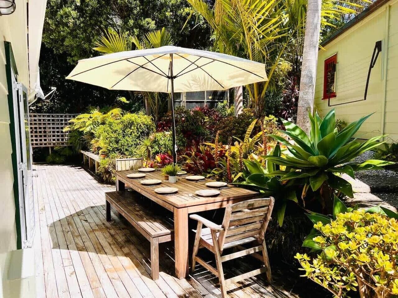 An outdoor wooden deck with a table and chairs, surrounded by tropical plants and a large umbrella.