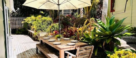 An outdoor wooden deck with a table and chairs, surrounded by tropical plants and a large umbrella.