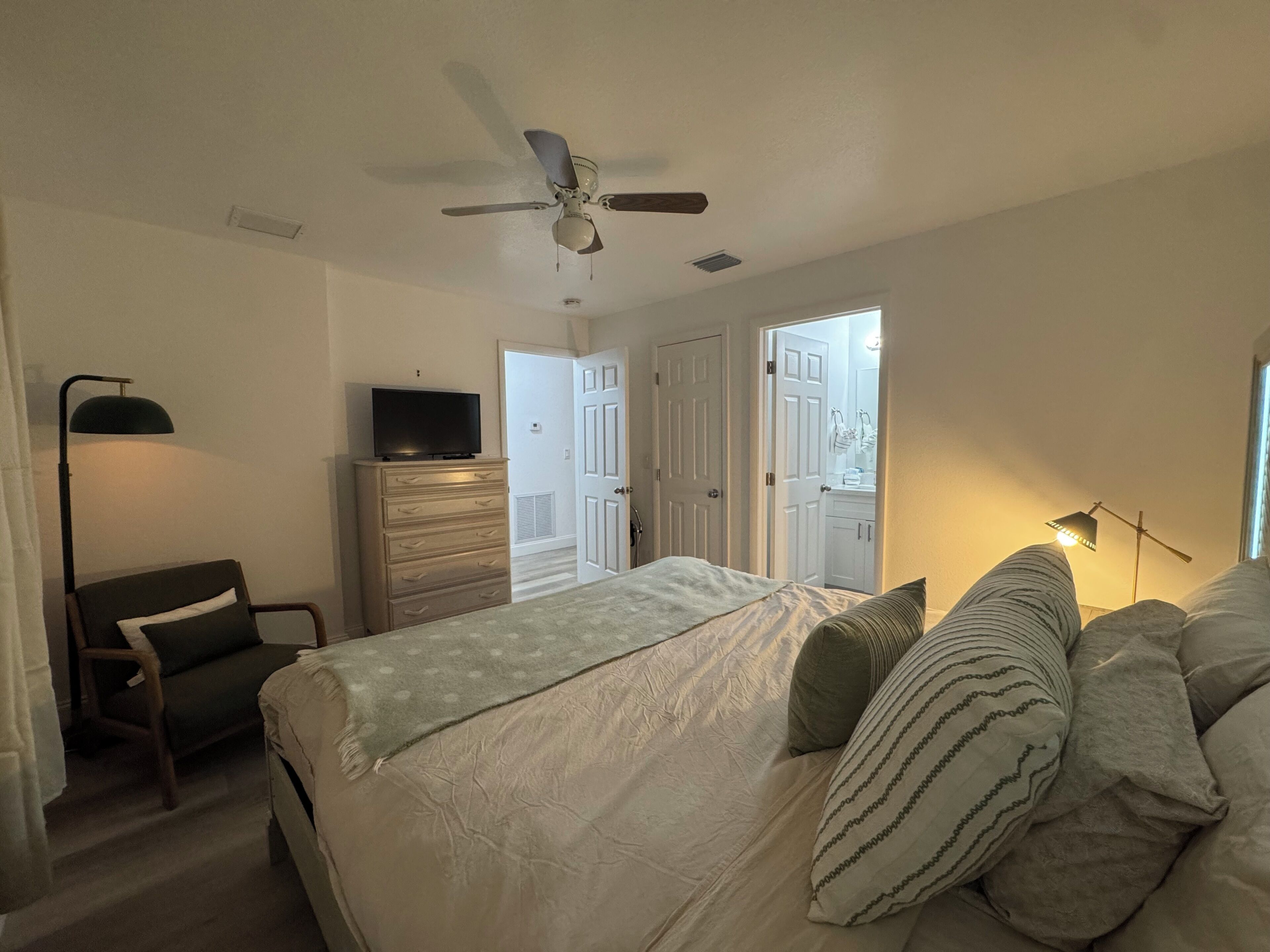 A bedroom with a bed, a dresser, a television, a chair, and a ceiling fan.