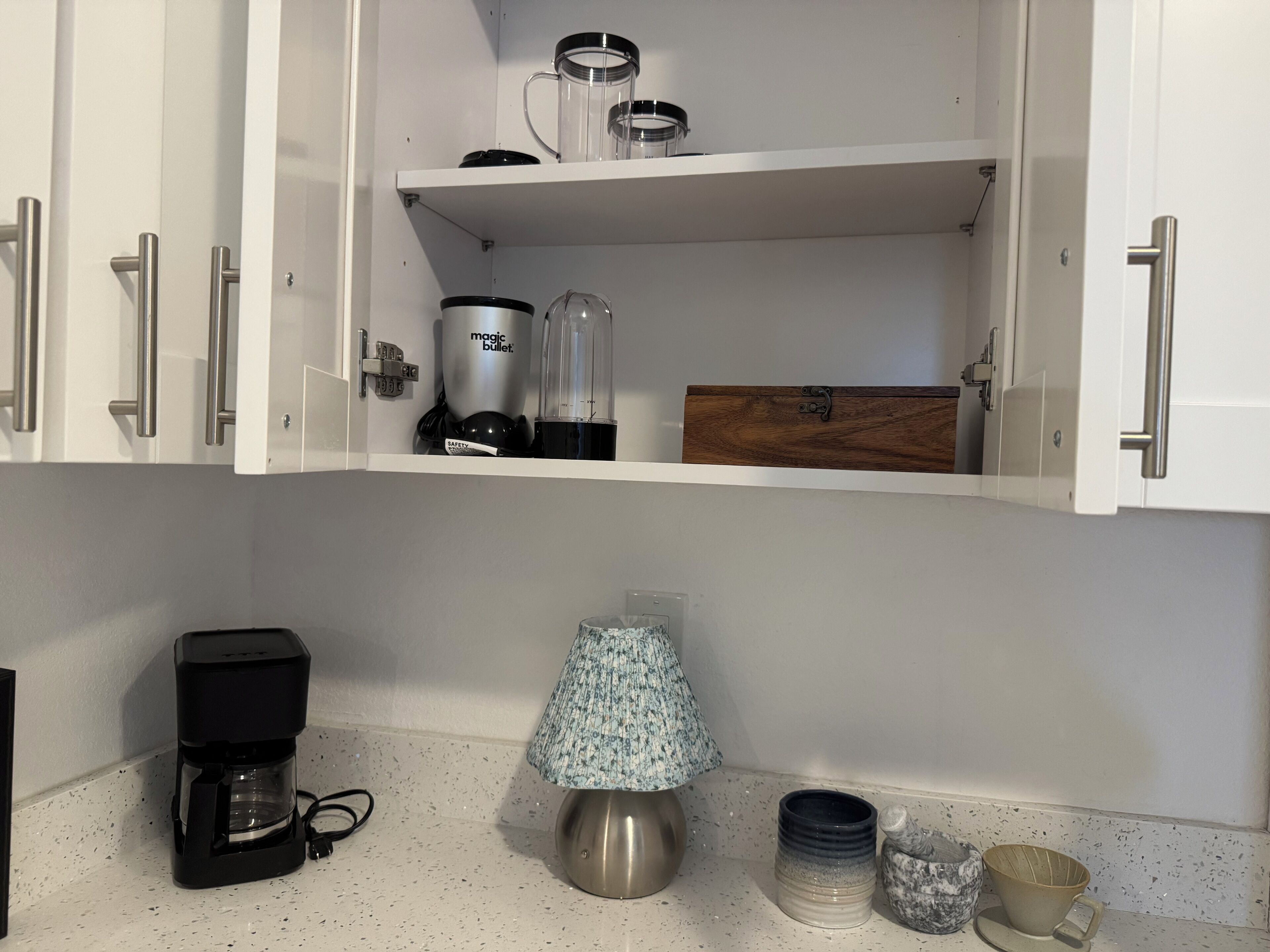 A kitchen with white cabinets, a coffee maker, a lamp, and a mug on the countertop.