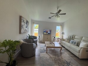 Una sala de estar con sofá, sillón, mesa de centro y ventilador de techo.