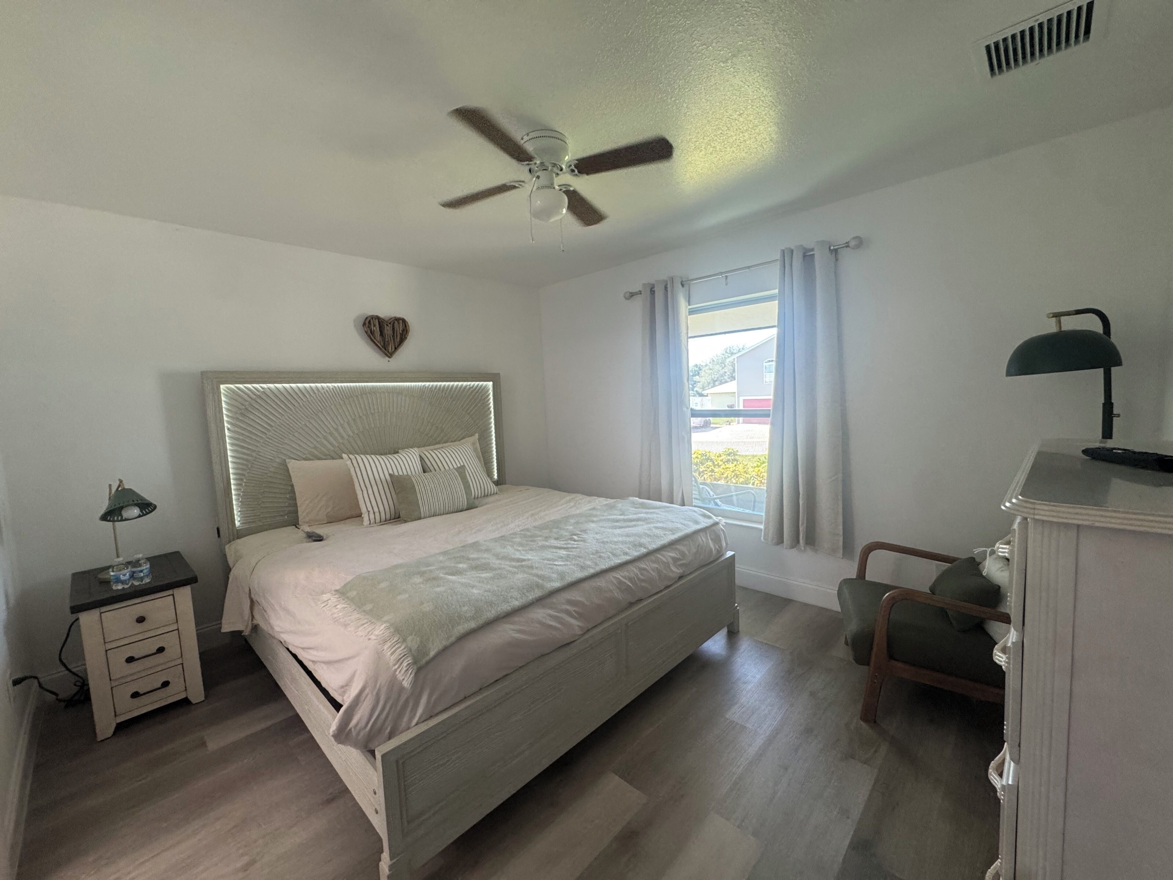 Une chambre à coucher comprenant un lit, une table de chevet, une lampe, une chaise et un ventilateur de plafond.