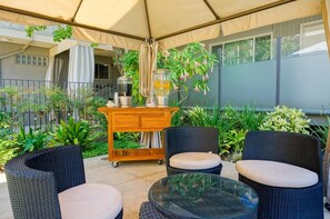 Eine Terrasse im Freien mit Korbmöbeln, einem Glastisch und einem Wagen mit Getränken.