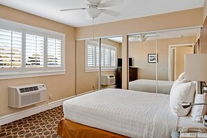 Ein Schlafzimmer mit einem Bett, einem Deckenventilator, einem Fenster mit Jalousien, einem Spiegel und einer Klimaanlage.