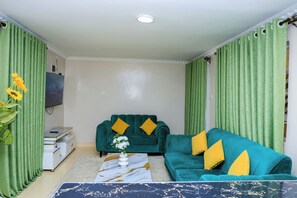 Ein Wohnzimmer mit einem türkisfarbenen Sofa, einem Couchtisch und grünen Vorhängen.