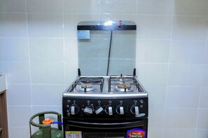 A kitchen with a gas stove, a gas cylinder, and a tiled wall.