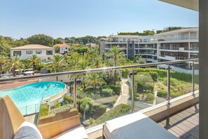 A balcony with a pool, lounge chairs, and a view of a modern building complex. - 4-room apartment in the luxury Parc du Cap residential complex (Antibes)
