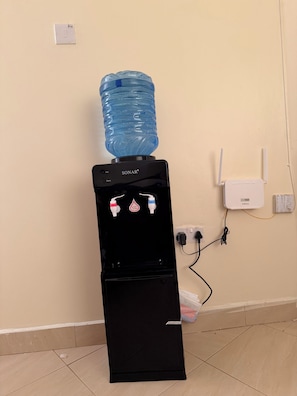 A SONAR water dispenser with a large water bottle on top, a power outlet, and a wall-mounted device on the wall. - Cozy Homes Airbn. 15 minutes from JKIA in Kasarani, Nairobi (Nairobi)