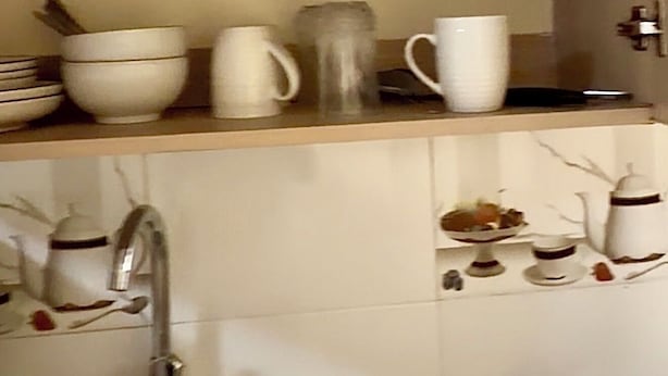 Eine Küche mit weißen Fliesen, einer Edelstahl-Spüle und verschiedenen weißen Küchenutensilien auf Regalen.
