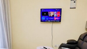 Ein Hotelzimmer mit Bett, Sofa, einem kleinen Tisch und einem am Wand montierten Fernseher, der Streaming-Dienste anzeigt.