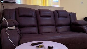 Ein braunes Ledersofa mit einer Fernbedienung und einer Flasche auf einem kleinen weißen Tisch.