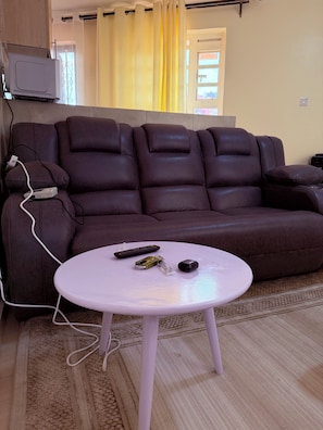 A brown leather sofa with a remote control and a bottle on a small white table. - Cozy Homes Airbn. 15 minutes from JKIA in Kasarani, Nairobi (Nairobi)