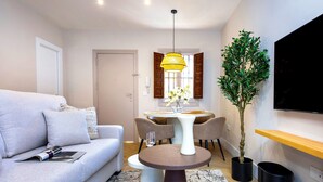 Een moderne woonkamer met een bank, een eettafel met stoelen, een potplant en een flatscreen televisie aan de muur.