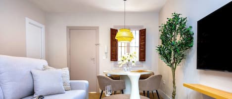 Un salon moderne avec un canapé, une table à manger et des chaises, une plante en pot et un téléviseur à écran plat fixé au mur.
