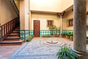 Ein Innenhof mit gefliestem Boden, einer Holztür, einer Treppe und Kübelpflanzen.