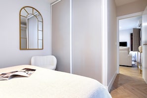 Ein modernes Schlafzimmer mit einem großen Bett, einem Spiegel und Blick in den Wohnbereich.