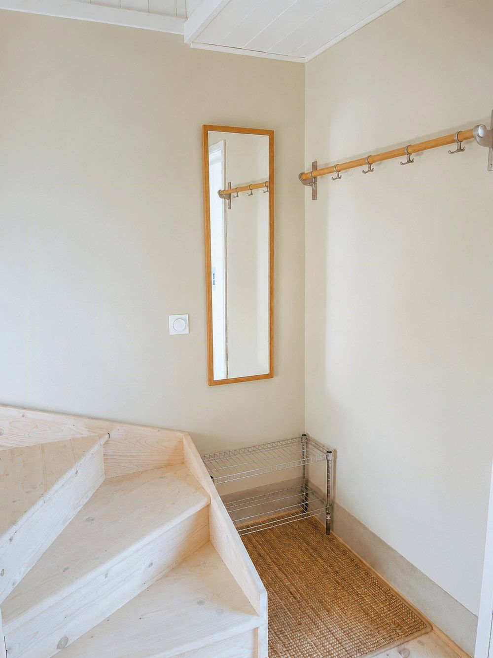 Une pièce avec un escalier en bois, une étagère en métal, un miroir et un porte-manteau.