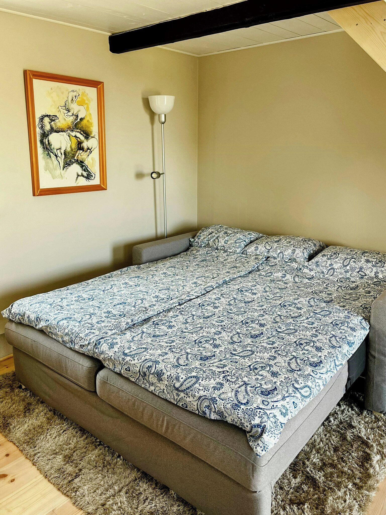 A room with a bed, a floor lamp, and a painting on the wall.
