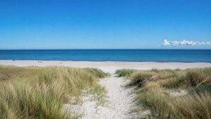 Una platja amb cel blau i un camí de sorra que porta a l'aigua.