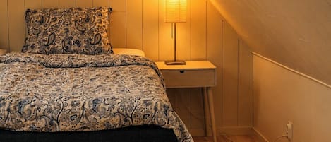 A bedroom with a bed, bedside table, lamp, and a chair.