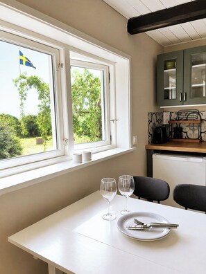 A dining area with a table set for two, a window with a view of greenery, and a kitchen area with cabinets and appliances. - Guest house among the apple orchards in Kivik (Kivik)
