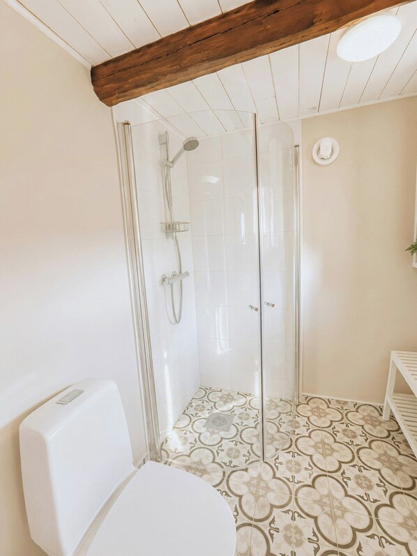 Een badkamer met een douche met glazen wand, toilet en vloertegels met een patroon.