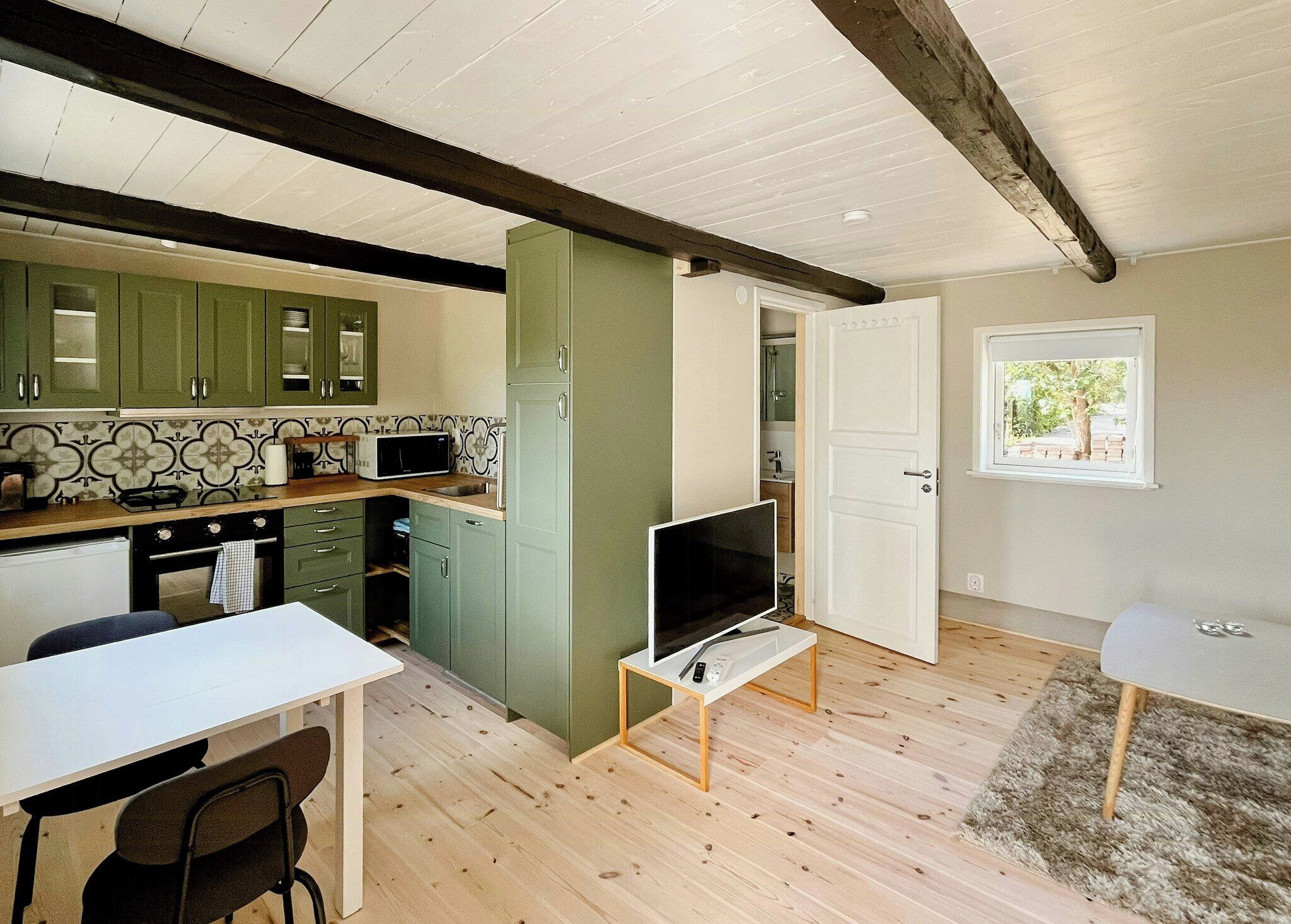 A compact kitchen with a microwave, stove, and cabinets. There's a dining area with a table and chairs, and a TV on a stand.
